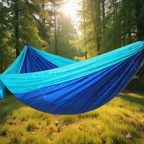Blue two-tone camping hammock hanging above a sunlit forest clearing