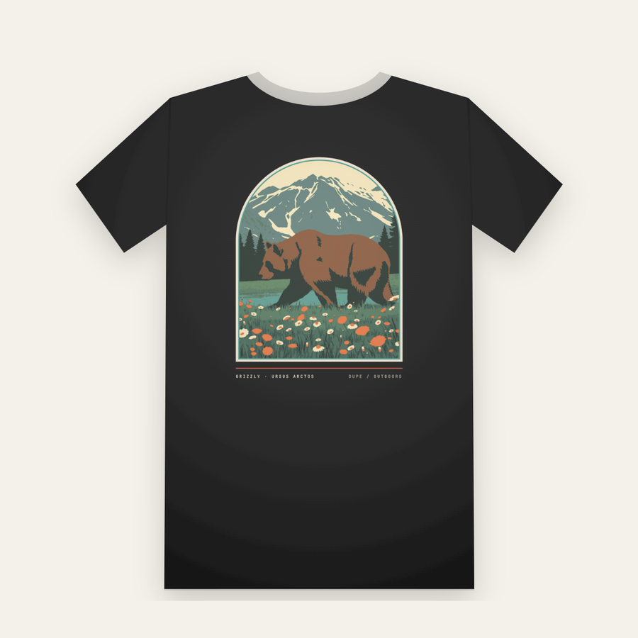 Black tee, back print: a grizzly bear in a wildflower meadow under a snowy peak, inside a large arch
