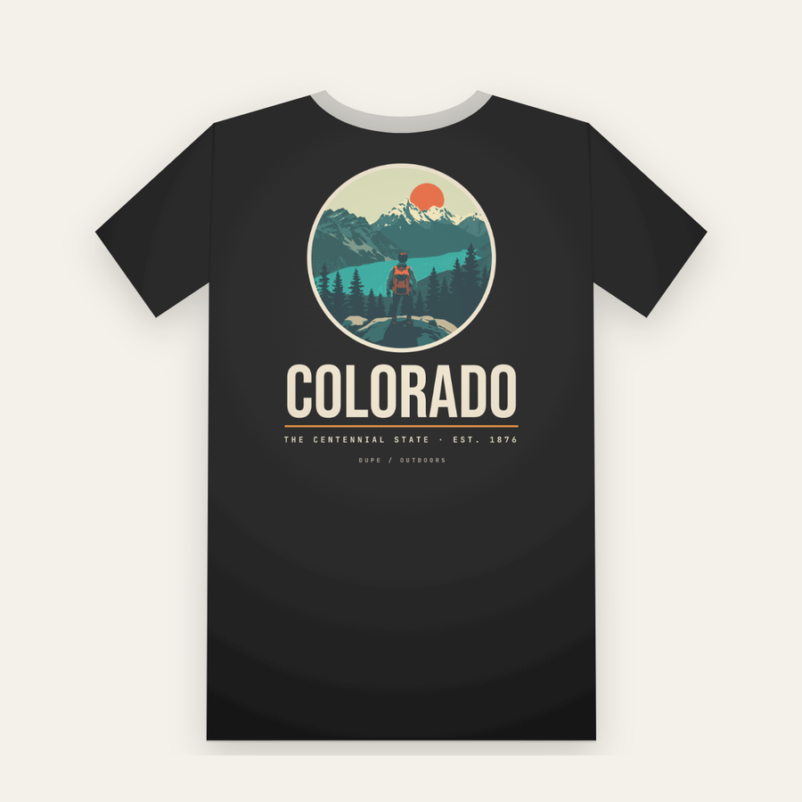 Black tee, back print: a hiker above a turquoise lake and snowy peaks in a circle, COLORADO below