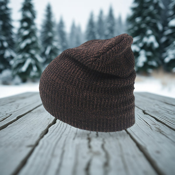 Brown knit beanie resting on a weathered wooden table, snowy pine forest behind