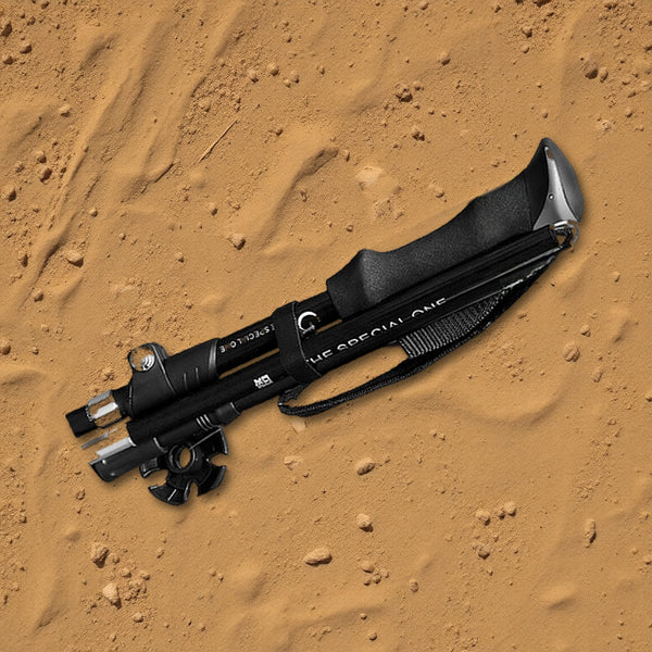 Black folding trekking pole, folded, lying on trail dirt