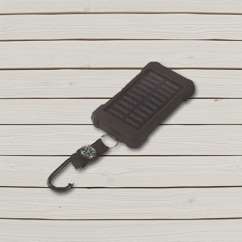 Black solar power bank with compass strap and carabiner lying on pale wooden boards