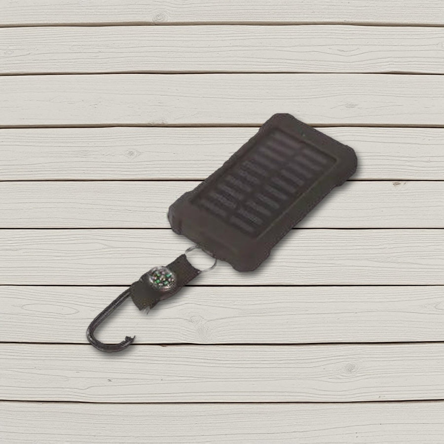 Black solar power bank with compass strap and carabiner lying on pale wooden boards