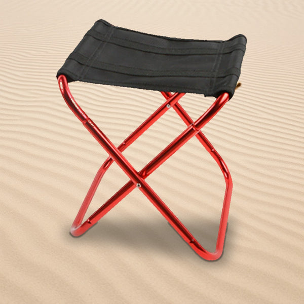 Folding camp stool with black seat and red aluminum legs standing on rippled sand