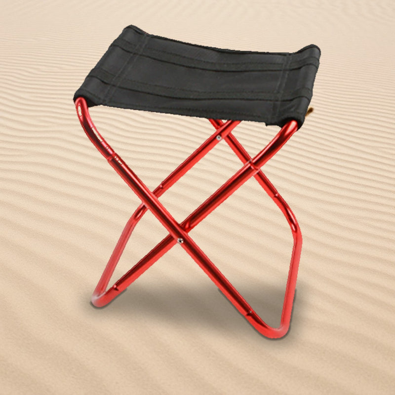 Folding camp stool with black seat and red aluminum legs standing on rippled sand